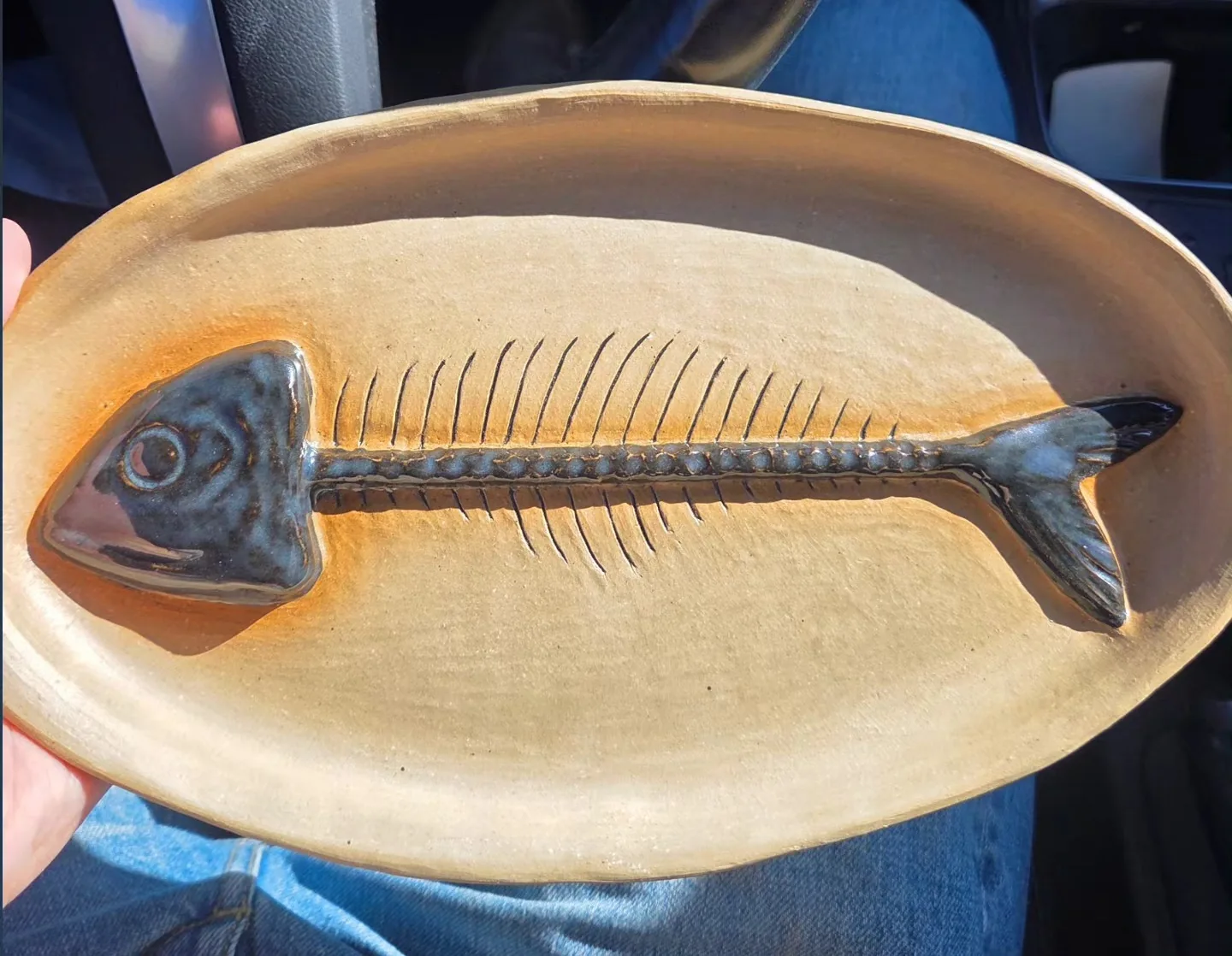 Oval stoneware platter with a fish skeleton carved and glazed dark blue into the surface, head and tail raised in relief.