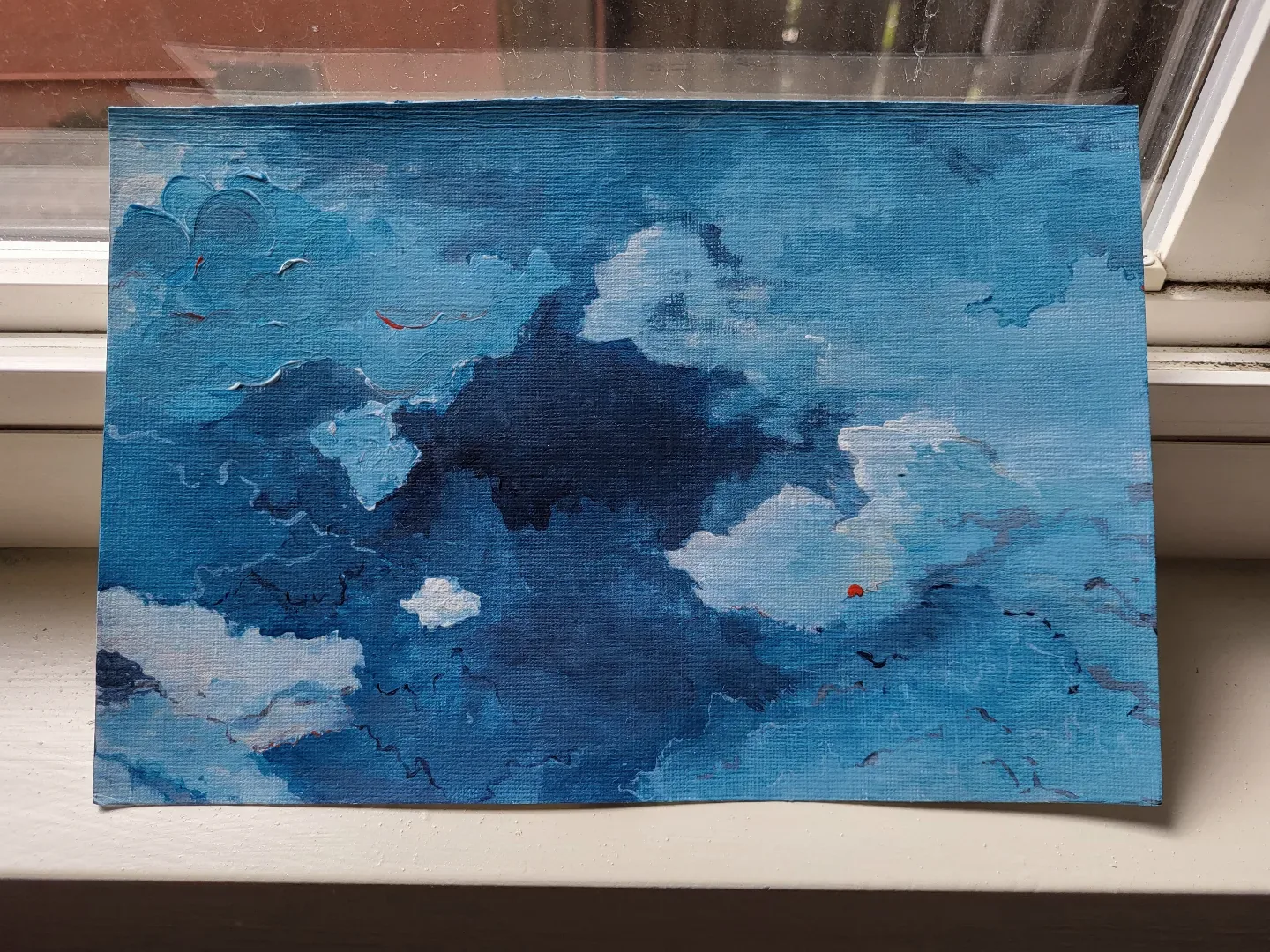 Small acrylic painting of a blue sky dense with clouds, a single speck of red near the centre right.